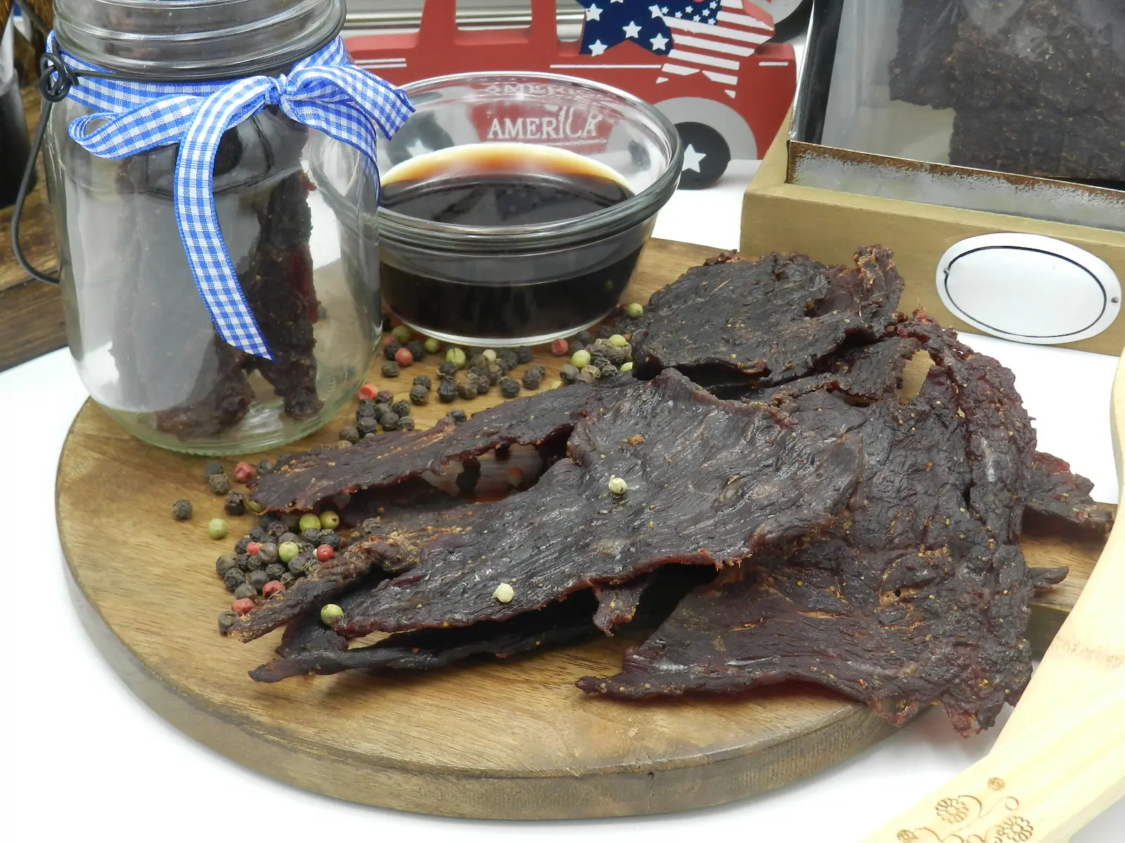 peppered jerky on a round wooded board with peppercorns adn a container of soy sauce